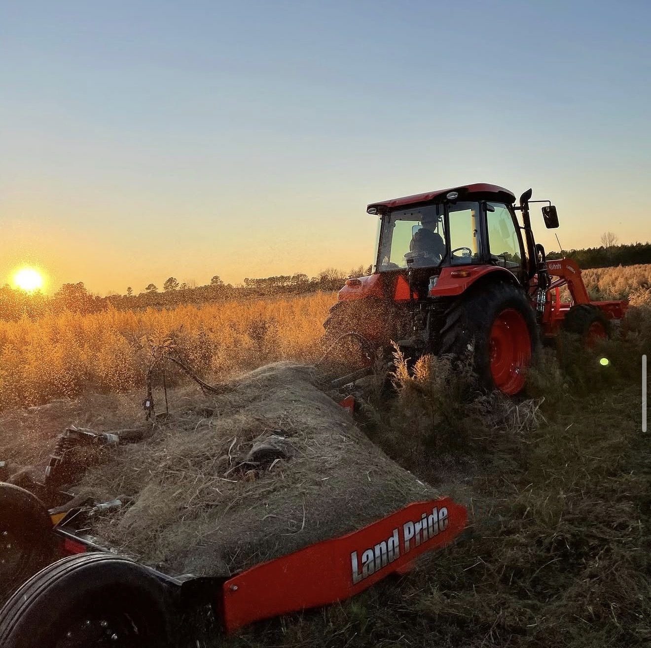 Tractor and mower cutting overgrown field at sunset