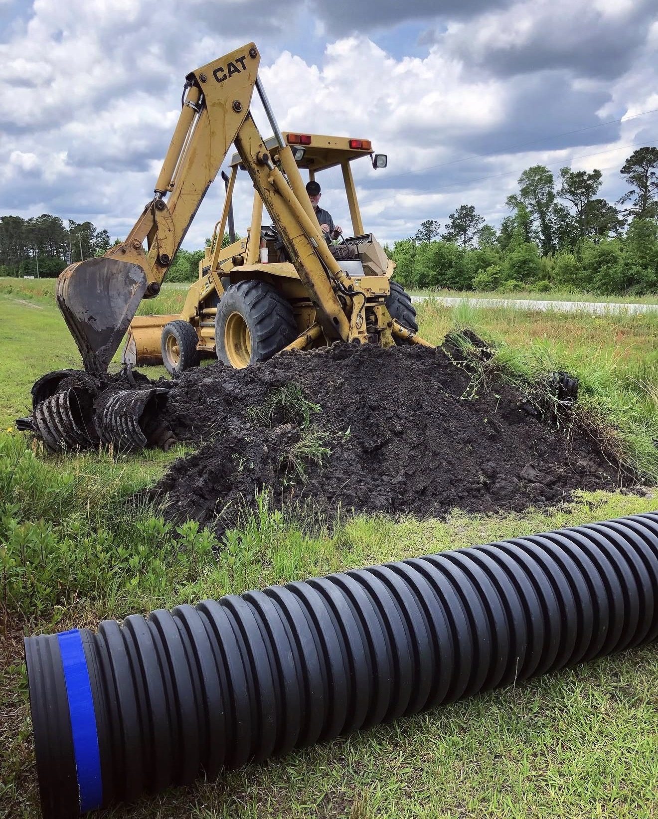 Backhoe digging a trench beside new drainage pipe